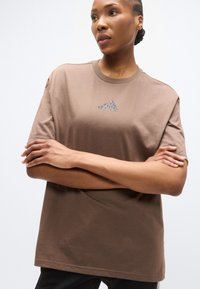 Καφέ βαμβακερό t-shirt με στρογγυλή λαιμόκοψη και κοντά μανίκια, με διακριτικό γκρι λογότυπο στο στήθος. Ομαλή υφή και άνετη εφαρμογή.