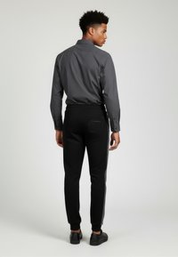 Mænds grå skjorte med knapper, parret med sorte joggers med en sidestribe og lomme på bagsiden, afsluttet med sorte sneakers.