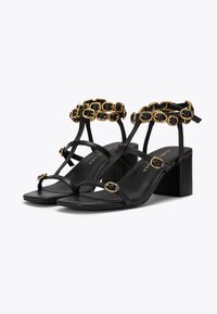 Czarne sandały na obcasie z blokowym obcasem, z złotą akcentującą paską z okrągłymi detalami. Gładka skórzana faktura i cienkie paski.