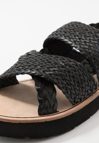 Schwarze geflochtene Sandalen mit einer dicken Plattform, strukturierten Riemen und einer hellen Fußbett. Hervorstechend ist ihr geflochtenes Design.