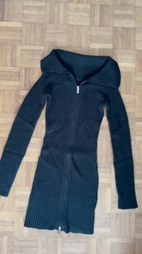 Schwarzes geripptes Strickkleid mit langen Ärmeln, schulterfreier Design, vollständigem Reißverschluss und taillierter Passform, flach auf einem Holzfußboden ausgelegt.