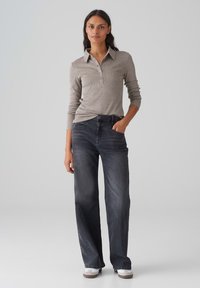 Hellgraues Langarm-Polohemd mit Knopfleiste, kombiniert mit locker sitzenden, dunkelgrauen Jeans. Der Look wird mit lässigen weißen Schuhen abgerundet.