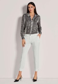 Zwart-wit slangenprint shirt met een knoopsluiting aan de voorkant, gecombineerd met witte slim-fit broeken en zwarte puntige hakken.