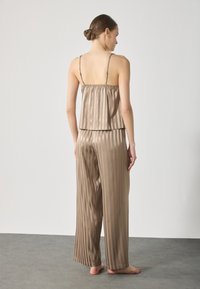 Satin sleepwear setti taupe-värissä, sisältäen laskostetun toppauksen, jossa on ohuet olkaimet, ja siihen sopivat leveälahkeiset housut, molemmat pehmeää tekstuuria.