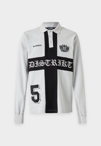 Polo blanc à manches longues avec motif croix noir, texte "DISTRIKT", numéro 5, écusson et marque "HAN KJØBENHAVN".