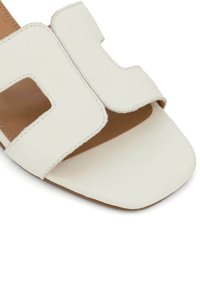Witte leren slidesandaal met uitgesneden ontwerp, vierkante neus en bruine binnenzool. Kenmerkt zichtbare stiksels en een gladde textuur.