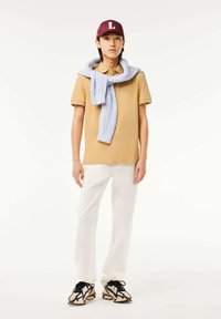 Gul polo skjorta, ljusblå stickad tröja knuten runt axlarna, vita byxor och mönstrade sneakers. Vinröd keps med en "L" detalj.