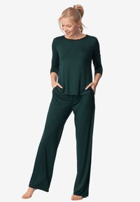 Zestaw odzieży dresowej w ciemnozielonym kolorze, składający się z bluzki z długim rękawem o falbaniastym dekolcie oraz dopasowanych, luźnych spodni z szerokimi nogawkami i kieszeniami.