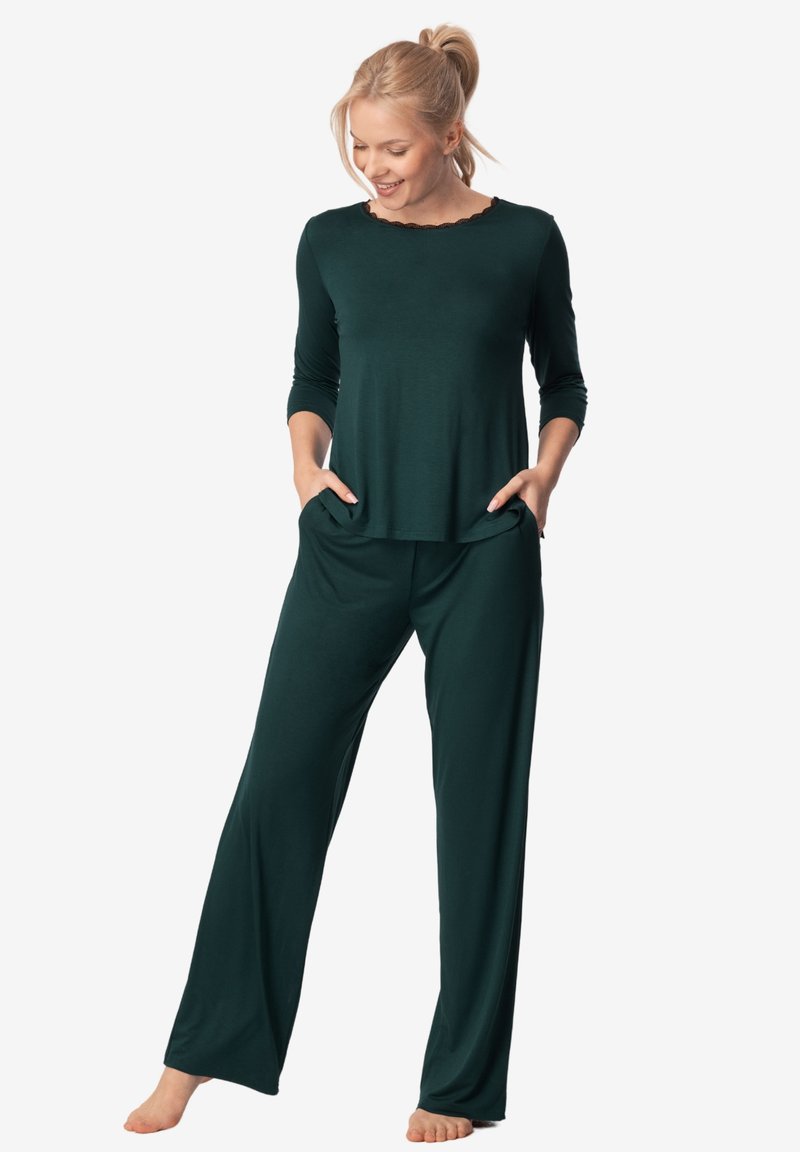 Zestaw odzieży dresowej w ciemnozielonym kolorze, składający się z bluzki z długim rękawem o falbaniastym dekolcie oraz dopasowanych, luźnych spodni z szerokimi nogawkami i kieszeniami.