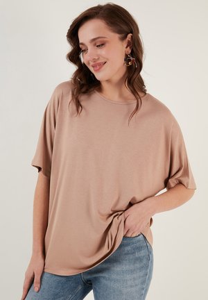 Light brown, short-sleeve, oversized t-shirt made of soft material, featuring a round neckline and a relaxed fit, paired with blue jeans.