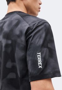 Gros plan d'une personne portant un t-shirt noir à manches courtes avec « TERREX » imprimé en blanc sur la manche.