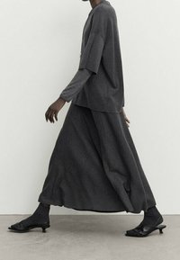 Pull en maille noir oversize et jupe longue en tissu texturé, assortis à des mules à talons noirs et des chaussettes assorties.