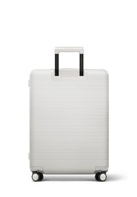 Valise rigide blanche avec des rainures horizontales, poignée rétractable noire et quatre roues pour la mobilité. Texture lisse.