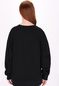 Felpa nera oversize con scollo rotondo e maniche lunghe. Texture morbida e polsini a costine, senza motivi o loghi visibili.