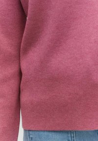 Tröja i ett mjukt, strukturerat, mörkröd tyg, med rundad halsringning och långa ärmar, kombinerad med ljusa denimjeans.