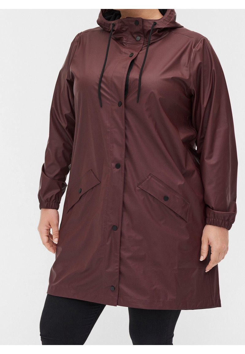 Vínová voděodolná pláštěnka s kapucí, elastickými manžetami a drukovými zapínáním; má dvě boční kapsy a hladký, lesklý povrch.
