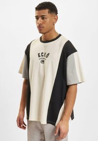 Short-sleeve T-shirt with a color-block design in cream, gray, and black. Features front logo print and relaxed fit, made from soft fabric.