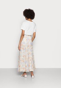 Witte t-shirt gecombineerd met een bloemen, gelaagde maxi rok met oranje, paarse en blauwe bloemen op een lichte achtergrond. Duidelijke blokhakken sandalen.