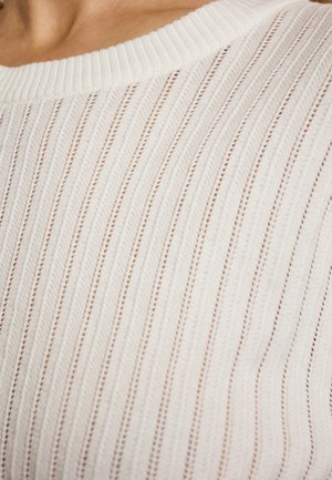 Pull en tricot couleur crème avec un motif en côtes verticales et de petites perforations, présentant un col rond et un détail textile texturé.