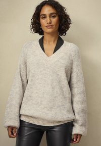 Crème v-hals trui met geribbelde textuur en oversized mouwen, gelaagd over een zwarte met kraag top. Zacht, cozy materiaal.