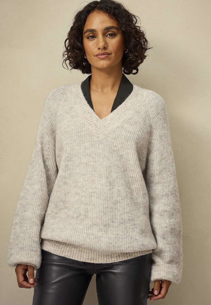 Crème v-hals trui met geribbelde textuur en oversized mouwen, gelaagd over een zwarte met kraag top. Zacht, cozy materiaal.