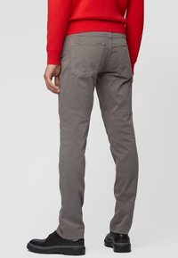Pantalones de mezcla de algodón gris con un corte ajustado, diseño de cinco bolsillos y bolsillos traseros de parche. Llevados con un suéter rojo y zapatos negros.