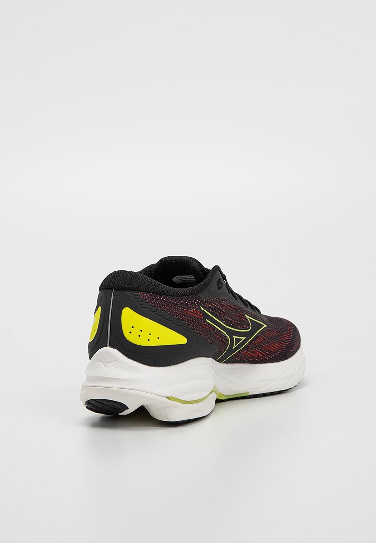 Zapatilla deportiva negra con parte superior texturada en rojo y negro, acentos amarillos y suela blanca. Cuenta con un collar acolchado y un diseño de cordones.