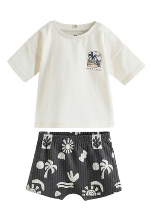 Cremefarbenes Kurzarmhemd mit Palmbaum- und Sonnenmotiv sowie "Take it Easy"-Text, kombiniert mit schwarzen Shorts mit weißen tropischen Prints.