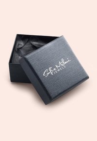 Svart texturerad smyckeslåda med en slät yta och en vit logotyp. Lådan är något öppen, vilket avslöjar skrumpnat svart silkespapper inuti.