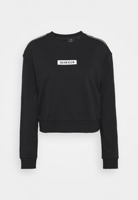 Sweat-shirt noir court à manches longues, avec un col rond, une étiquette blanche portant "CALVIN KLEIN" et des rayures discrètes sur les épaules.