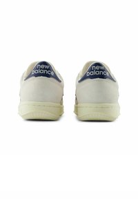 Valkoiset mokkanahkaiset tennarit, joissa on laivastonsininen kantapääosa ja "new balance" -logo, teksturoitu kumipohja, minimalistinen muotoilu ja pyöreä muoto.