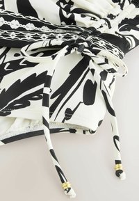 Schwarz-weiß gemusteter Stoff mit einem Tunnelzug an der Taille, verziert mit goldfarbenen Akzenten und einer weichen, glatten Textur.