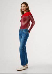 Top de manga larga de rayas rojas y negras, con diseño ajustado, combinado con jeans rectos de mezclilla azules y zapatillas blancas con cordones.