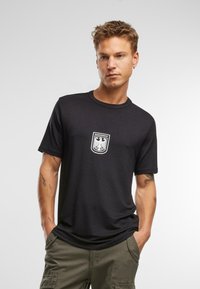 Fekete pamut póló rövid ujjakkal, fehér Bundeswehr logóval a mellrészen és kerek nyakkivágással.