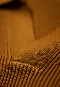 Tissu en tricot marron présentant une texture côtelée et une surface lisse, mettant en valeur un mélange de nuances claires et plus foncées dans le matériau.