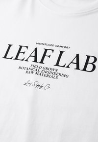 Tissu blanc avec texte imprimé en noir : "CONFORT INÉGALÉ LEAF LAB CULTIVÉ EN CHAMP INGÉNIERIE BOTANIQUE MATIÈRES PREMIÈRES Leaf Supply Co."