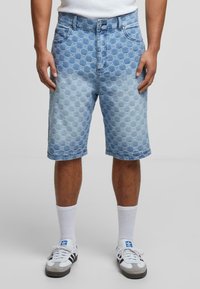 Lyseblå denimshorts med et geometrisk præget mønster, i en klassisk pasform med oprullede kanter, parret med hvide ankelsokker og sneakers.
