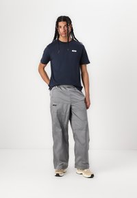 Navy t-shirt with a small logo, paired with light gray, loose-fitting cargo pants featuring pockets and a textured surface.