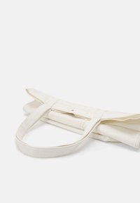 Canvas tote bag i off-white, med två hållbara handtag och synliga söm detaljer. Designen är vikbar för kompakt förvaring.