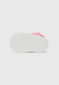 Pink sneaker with textured upper, white rubber outsole featuring a circular logo. Design includes prominent stitching and a padded collar.