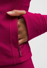 Fuksiaroosa spordijakk lukustatava tasku ja sõrmeava detailiga, sujuva kangaga ja lameõmblustega, mis tagavad stiilse istuvuse.