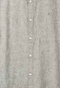 Beige painettu paita, jossa ohuita valkoisia pystysuoria raitoja ja hienovarainen kirjailtu logo rinnassa.