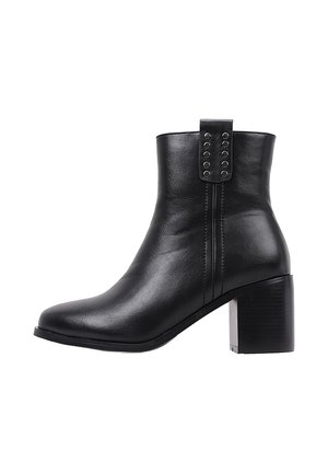 Bottine noire en cuir avec talon carré et œillets décoratifs en métal sur la languette de tirage, vue de côté sur fond blanc.