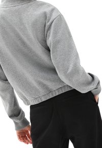 Gray cropped sweatshirt with a textured fabric, ribbed cuffs, and hem, paired with black pants featuring back pockets.