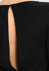 Prenda negra con un diseño de escote en V profundo en la parte espalda y un pequeño cierre de botón en el cuello, confeccionada en una tela suave y texturizada.