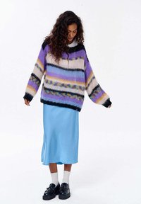 Pletený sveter so špurple, čiernymi a krémovými pruhmi, skombinovaný s svetlomodrou saténovou sukňou, doplnený čiernymi loafers a bielymi ponožkami.