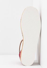 Sandale avec semelle blanche texturée, matériaux supérieurs beige et rouge, positionnée verticalement contre un fond d'angle blanc.