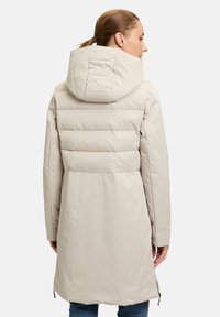 Manteau matelassé beige clair avec une capuche, présentant des quadrillages horizontaux, une coupe droite et des poches latérales zippées. Tissu lisse et résistant à l'eau.