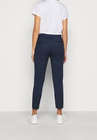 Pantaloni navy blue su misura con vestibilità slim, dotati di due tasche posteriori e una texture morbida, abbinati a sneaker platform bianche.