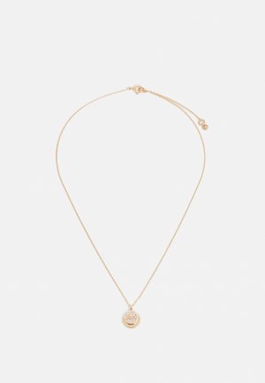 Delicate gold chain necklace with round pendant featuring an intricate cutout floral design and a small circular tag near the clasp.